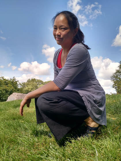 Photo of smiling Asian woman on green grass under blue sky and clouds